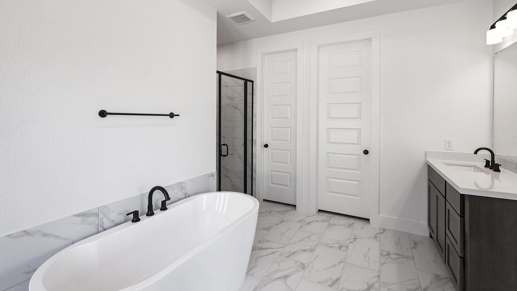 Full bath featuring marble finish floor, visible vents, a freestanding bath, a stall shower, and vanity