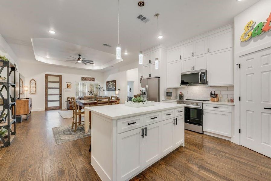 Kitchen with stainless steel appliances, white cabinets, a center island, ceiling fan, and tasteful backsplash