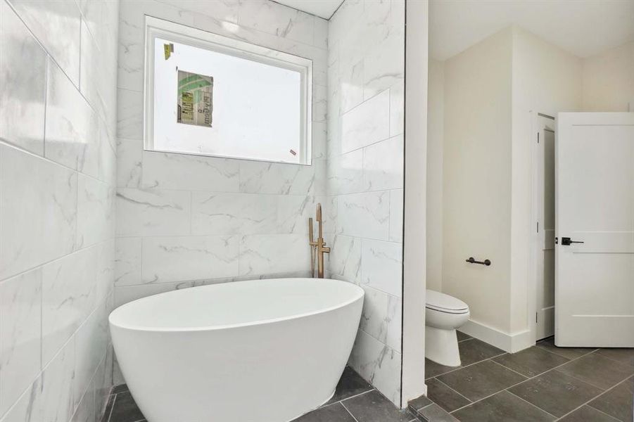 Bathroom featuring tile walls, a washtub, and toilet