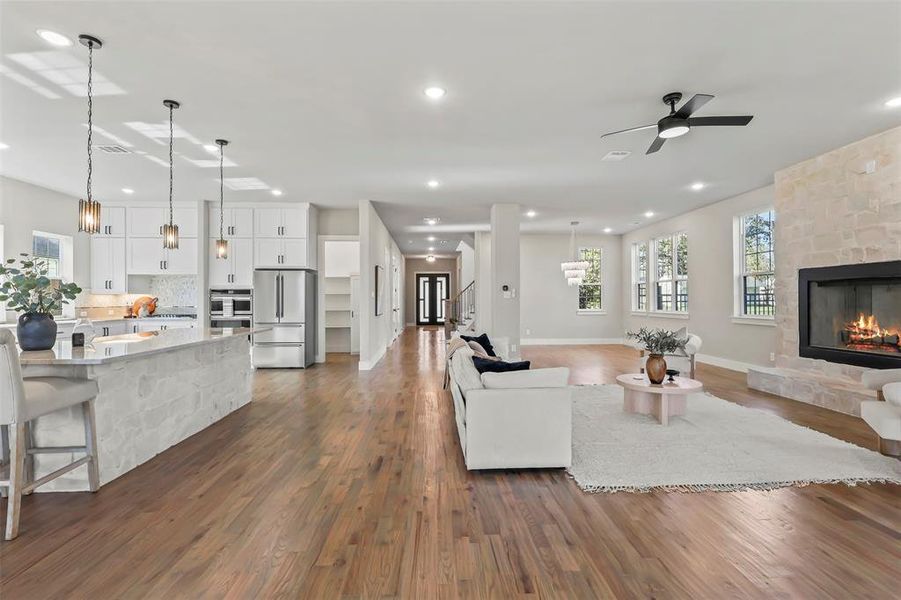 Living area featuring a stone fireplace, dark wood-style floors, ceiling fan, recessed lighting, and stairway Living area featuring a stone fireplace, dark wood-style floors, ceiling fan, recessed lighting, and stairway