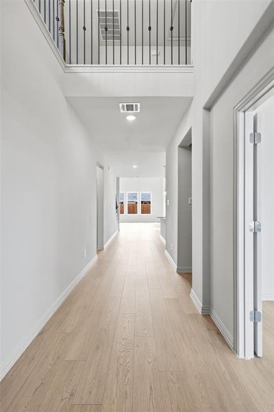 Hallway with a high ceiling, light wood-style floors, and recessed lighting