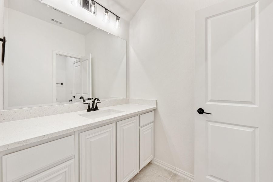 Bathroom vanity with white cabinets, quartz countertop, large mirror, and black fixtures