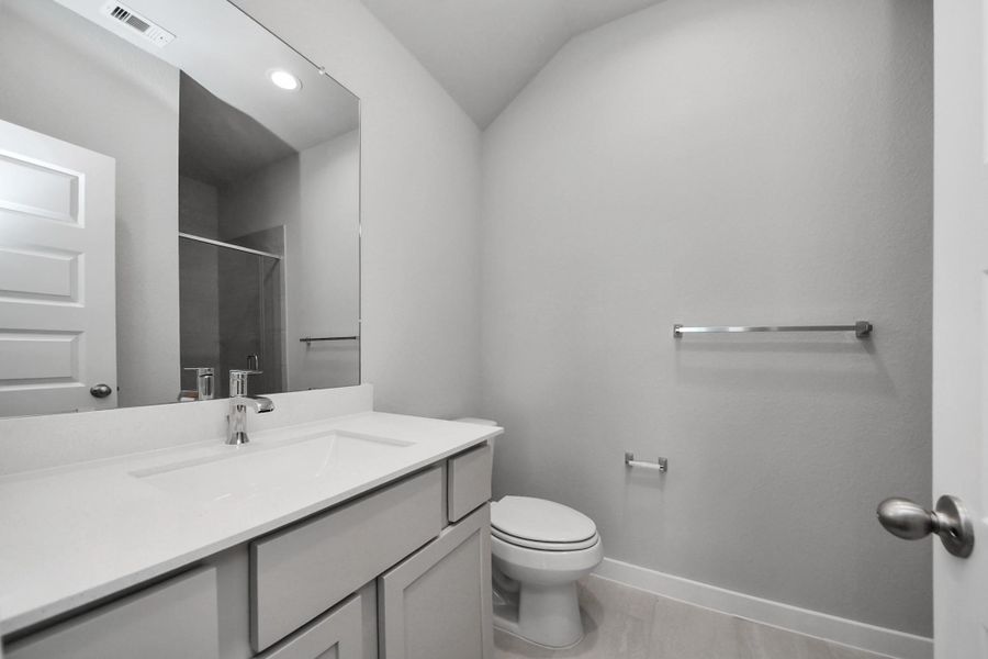 Secondary bath features tile flooring, a walk-in shower tile surround, light stained wood cabinets, beautiful light countertop. Sample photo of completed home with similar floor plan. Actual colors and selections may vary.