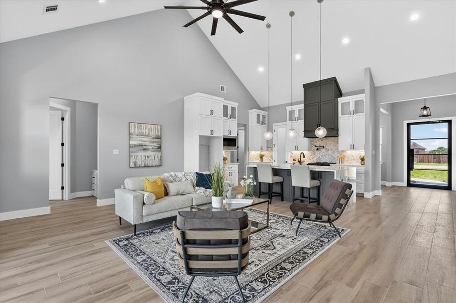 Open-concept living area featuring vaulted ceilings, wood-finish flooring, recessed lighting, a ceiling fan, and a kitchen with an island, pendant lights, and a range hood