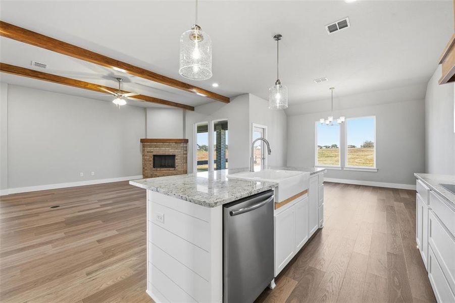 Kitchen featuring white cabinetry, stainless steel dishwasher, a fireplace, hanging light fixtures, and open floor plan