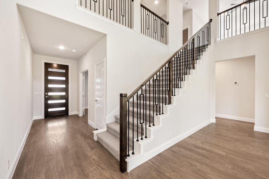 Two-story foyer with wood staircase, iron balusters, hardwood floors, and dark front door with glass panels Two-story foyer with wood staircase, iron balusters, hardwood floors, and dark front door with glass panels