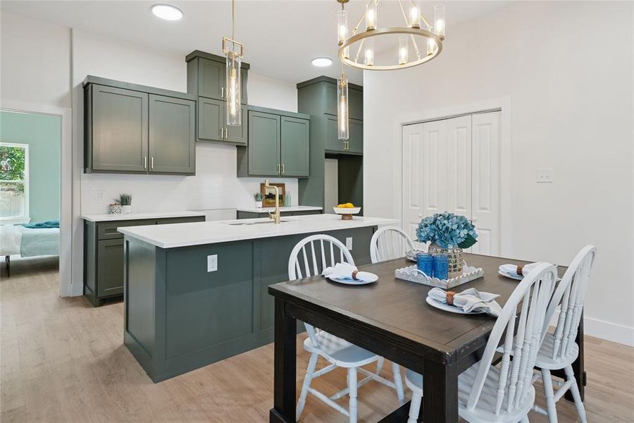 Kitchen featuring green cabinets, a chandelier, light wood finished floors, a center island with sink, and decorative light fixtures