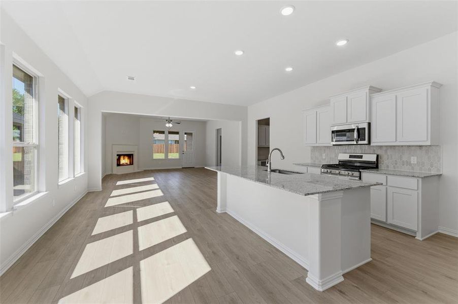 Kitchen with a lit fireplace, white cabinetry, stainless steel appliances, light stone counters, and a center island with sink