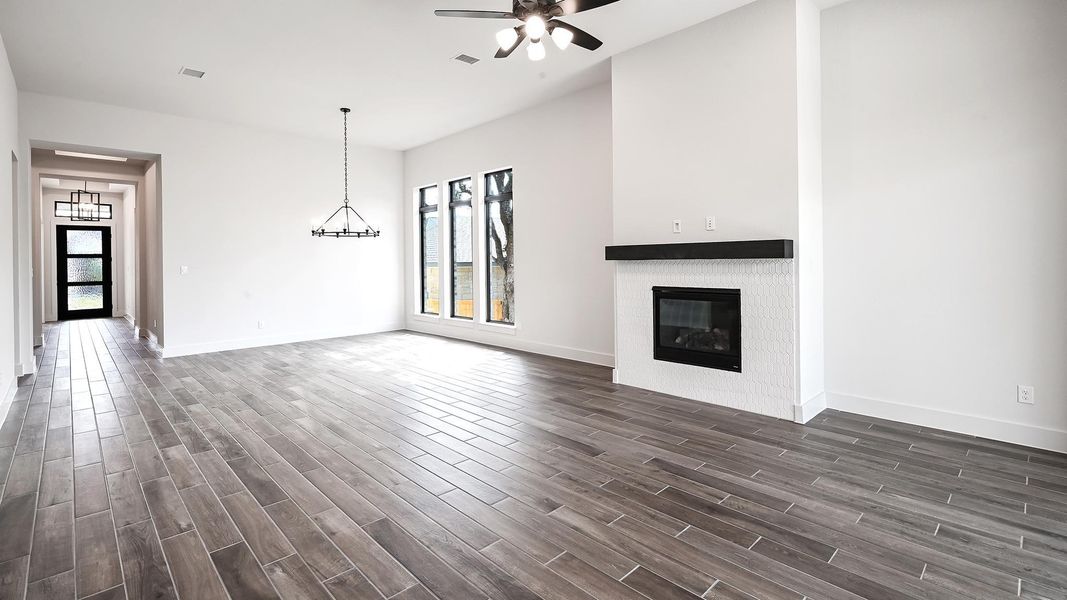 Unfurnished living room featuring a glass covered fireplace, dark wood-type flooring, and ceiling fan