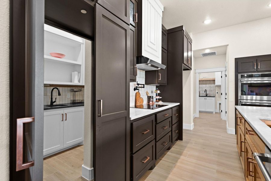 Kitchen with stainless steel double oven, decorative backsplash, light wood-type flooring, ventilation hood, and a sink Kitchen with stainless steel double oven, decorative backsplash, light wood-type flooring, ventilation hood, and a sink
