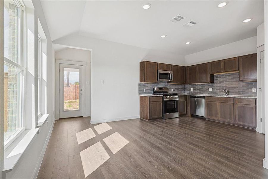 Kitchen with hardwood / wood-style floors, appliances with stainless steel finishes, sink, dark brown cabinets, and tasteful backsplash