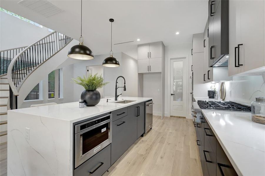 Kitchen with pendant lighting, white cabinetry, an island with sink, sink, and light wood-type flooring