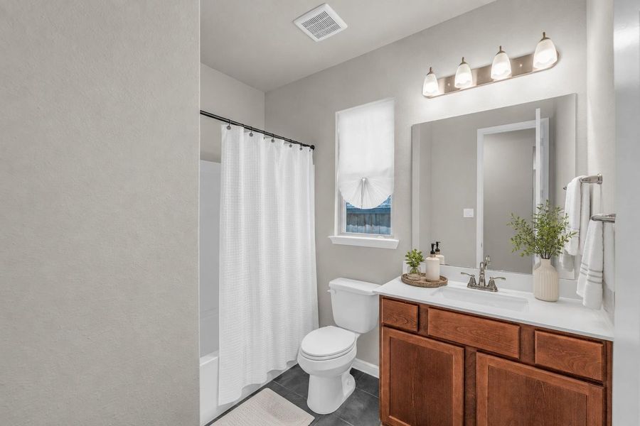 Well-appointed secondary bathroom with a rich wood vanity, dark tile flooring, and a tub-shower combination. Well-appointed secondary bathroom with a rich wood vanity, dark tile flooring, and a tub-shower combination.