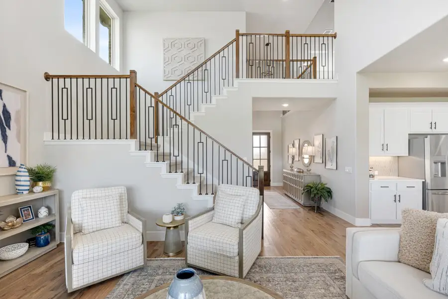 Open living room with two-story staircase, wood and iron railing, hardwood floors, and seating area