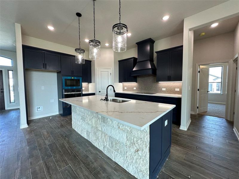 Kitchen with dark wood finished floors, light stone counters, custom range hood, dark cabinetry, and recessed lighting Kitchen with dark wood finished floors, light stone counters, custom range hood, dark cabinetry, and recessed lighting