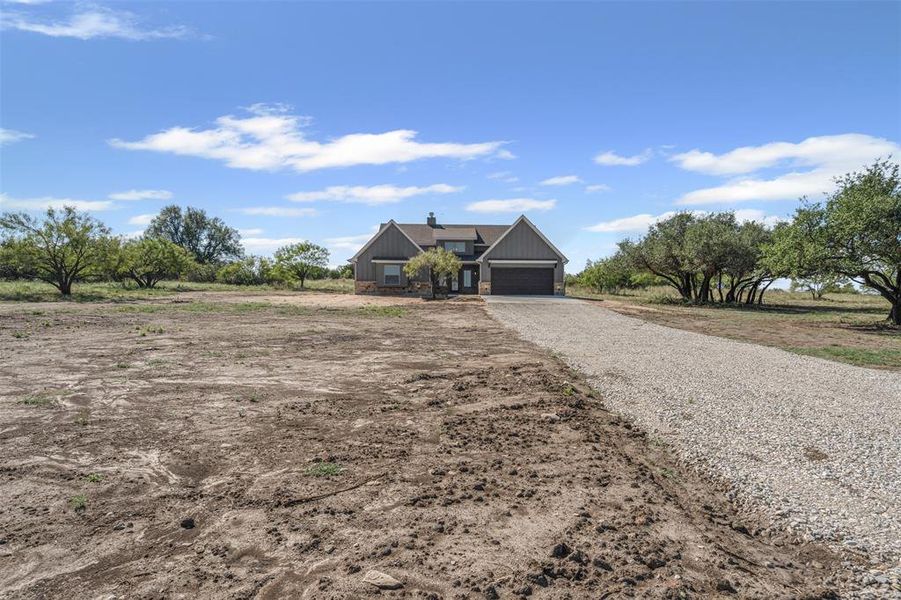 View of front of home with gravel driveway, a chimney, board and batten siding, and a view of rural / pastoral area