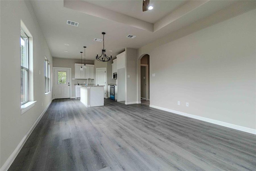 Unfurnished living room with an inviting chandelier, a tray ceiling, sink, and light hardwood / wood-style flooring