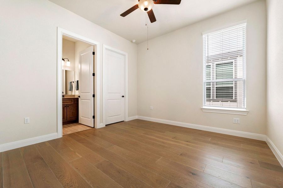 Well-lit room with wood flooring, equipped with a cooling ceiling fan and a nearby bathroom. Well-lit room with wood flooring, equipped with a cooling ceiling fan and a nearby bathroom.