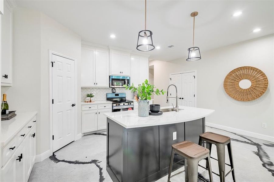 Kitchen featuring decorative backsplash, white cabinets, stainless steel appliances, and an island with sink