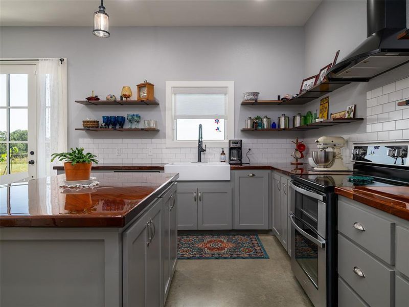 Kitchen with double oven range, wall chimney exhaust hood, butcher block counters, gray cabinets, and backsplash Kitchen with double oven range, wall chimney exhaust hood, butcher block counters, gray cabinets, and backsplash
