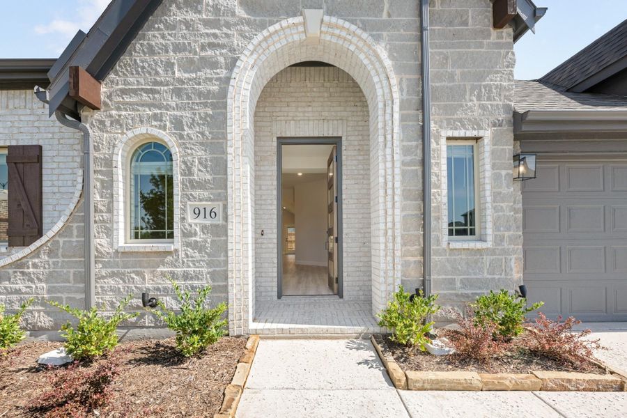 Home entrance with arched brick doorway, open front door, and landscaped walkway at number 916