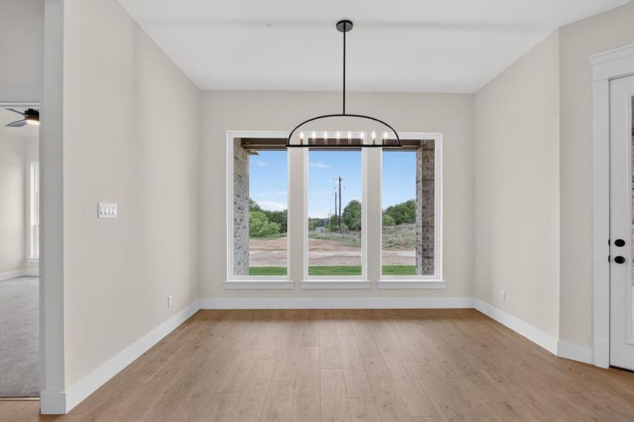 Spacious room featuring wood-finish flooring, light-colored walls, and a modern black chandelier Spacious room featuring wood-finish flooring, light-colored walls, and a modern black chandelier