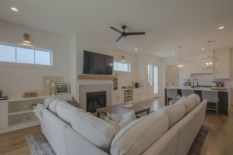 Living room with ceiling fan with notable chandelier, a healthy amount of sunlight, a fireplace, and light hardwood / wood-style flooring