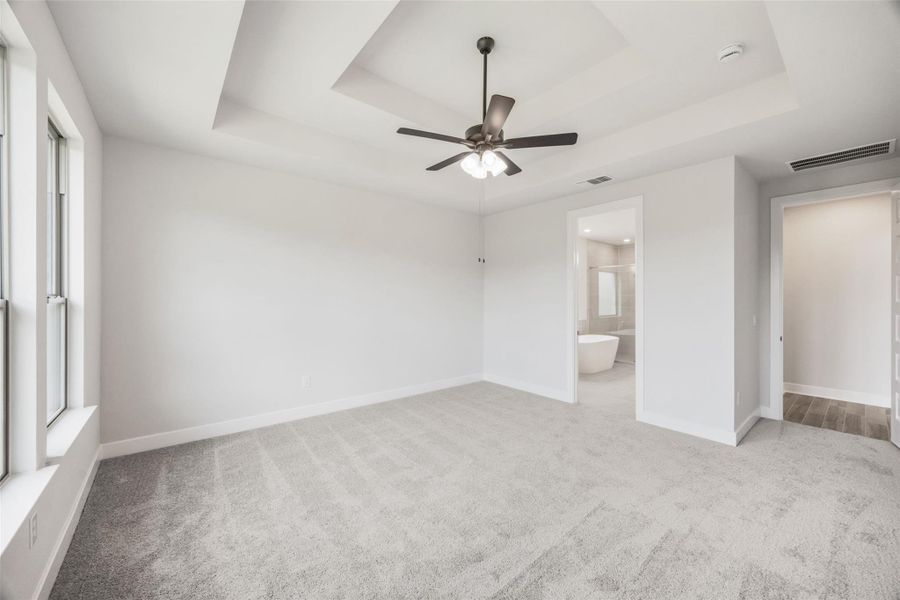 Unfurnished bedroom with a raised ceiling, light carpet, a ceiling fan, and connected bathroom Unfurnished bedroom with a raised ceiling, light carpet, a ceiling fan, and connected bathroom