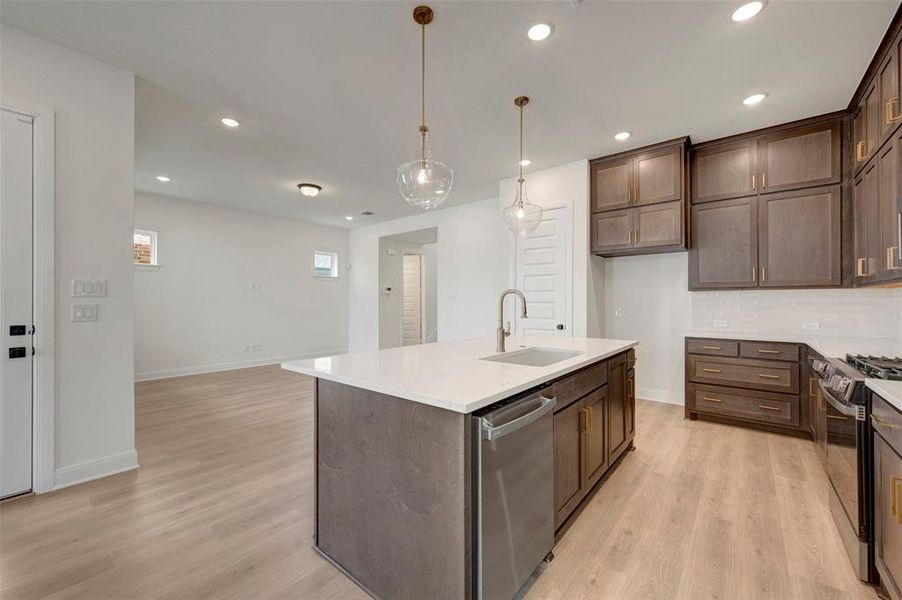 Kitchen featuring a central island with an undermount sink, pendant lighting, stainless steel dishwasher, and quartz countertop