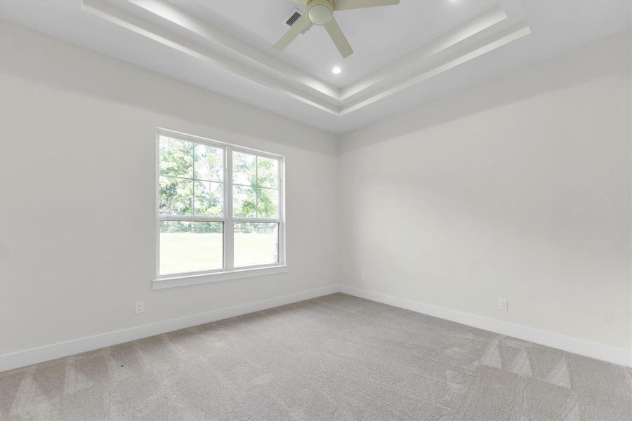 This is a modern farmhouse-style home with a spacious green lawn, large windows, and a covered entryway. It has a combination of white siding with black trim and a gabled roof, set against a backdrop of mature trees.