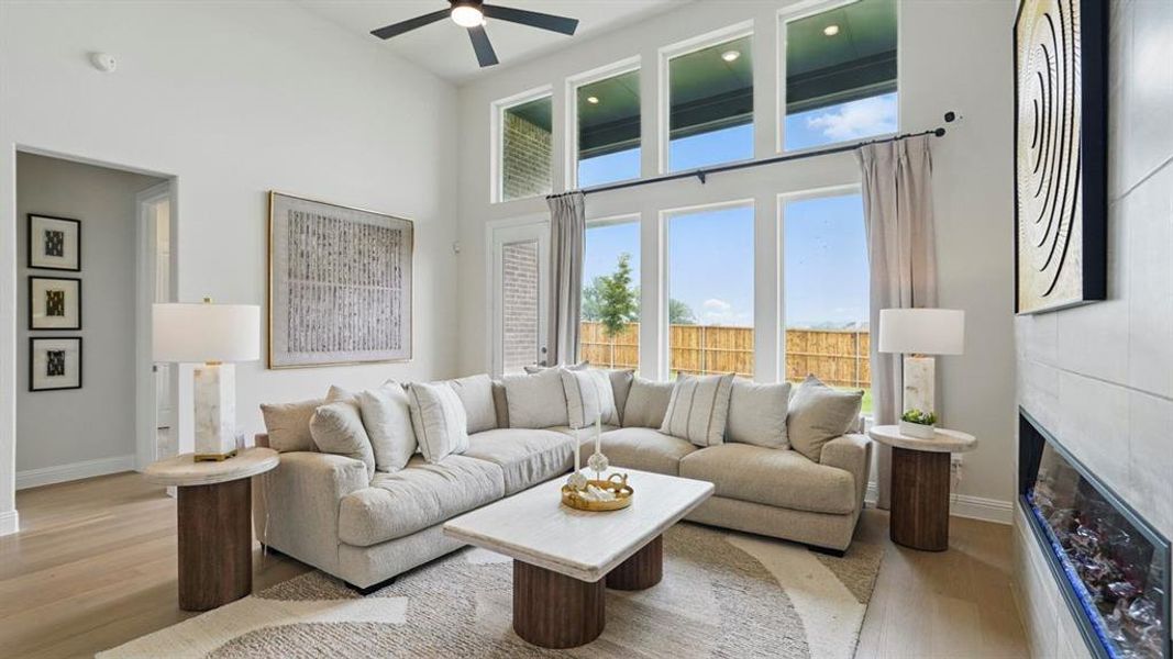 Living room with a high ceiling, a tiled fireplace, light wood finished floors, and ceiling fan