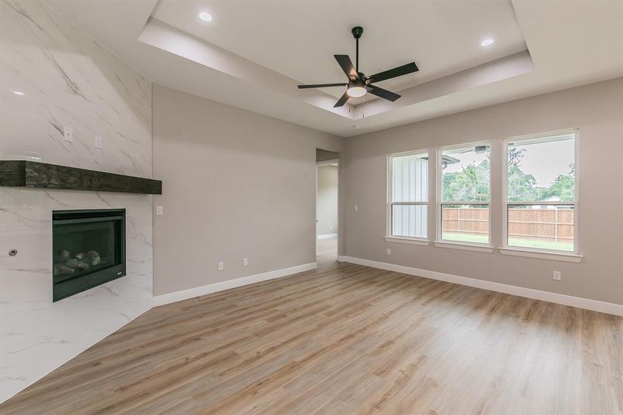 Unfurnished living room with a tray ceiling, a ceiling fan, light wood-style floors, and recessed lighting Unfurnished living room with a tray ceiling, a ceiling fan, light wood-style floors, and recessed lighting