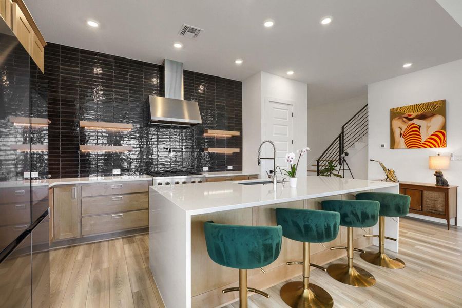 The chef's kitchen with glossy black subway tile backsplash and warm wood flooring offers a sophisticated upgrade.