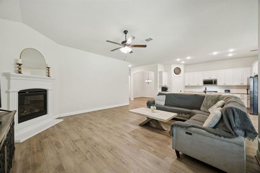 Open concept living room with luxury vinyl plank flooring, ceiling fan, and a gas fireplace.