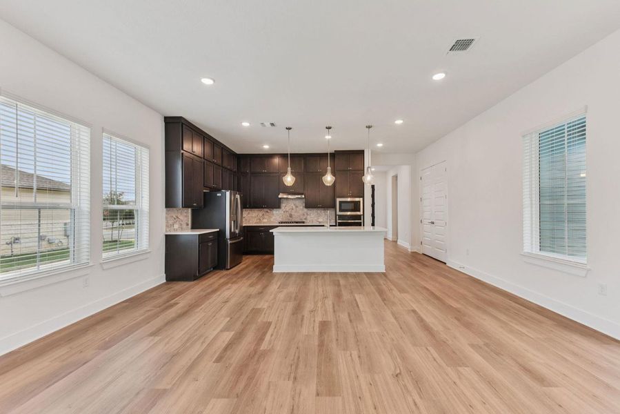 Open-concept living area with wood-finish flooring, recessed lighting, and multiple windows with blinds