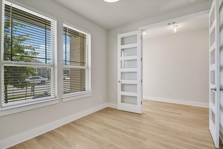 Double glass doors open to a flexible room featuring natural wood flooring and clean lines. Double glass doors open to a flexible room featuring natural wood flooring and clean lines.