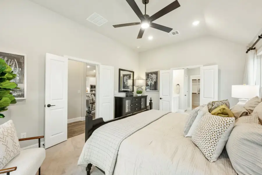 Spacious master bedroom with ceiling fan, neutral tones, and doors leading to bathroom and walk-in closet