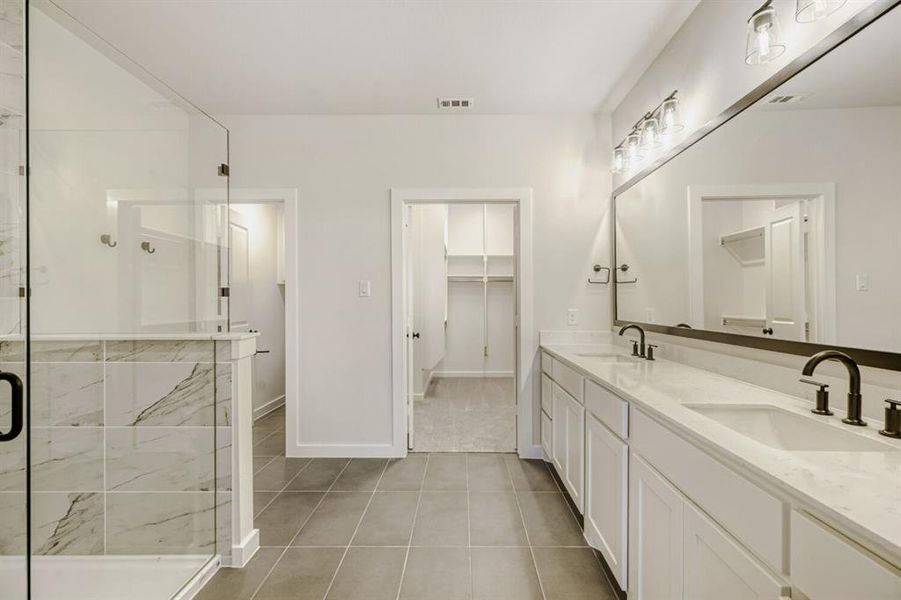 Bathroom featuring double vanity, a stall shower, light tile patterned floors, and a spacious closet
