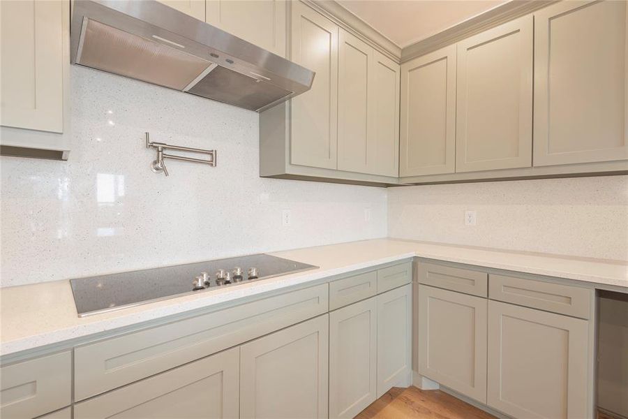 Kitchen featuring under cabinet range hood, light stone countertops, backsplash, black electric stovetop, and light wood-style floors