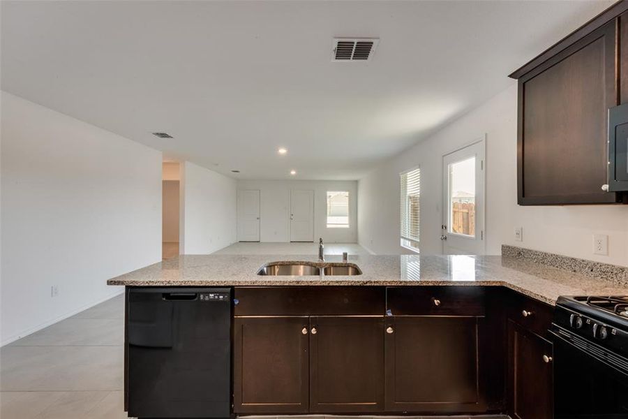 Kitchen featuring dark brown cabinets, black appliances, light stone counters, recessed lighting, and open floor plan Kitchen featuring dark brown cabinets, black appliances, light stone counters, recessed lighting, and open floor plan