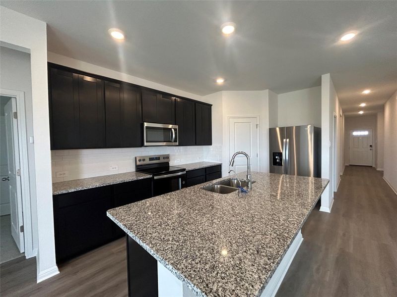 Kitchen featuring dark wood-style floors, dark cabinetry, stainless steel appliances, tasteful backsplash, and an island with sink Kitchen featuring dark wood-style floors, dark cabinetry, stainless steel appliances, tasteful backsplash, and an island with sink