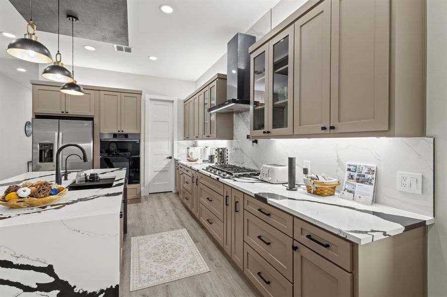 Kitchen with pendant lighting, light stone countertops, glass insert cabinets, decorative backsplash, and appliances with stainless steel finishes