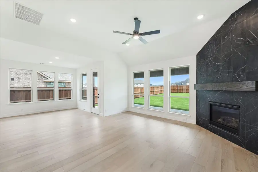 Open living room with light hardwood floors, vaulted ceiling, and dark tile fireplace accent wall