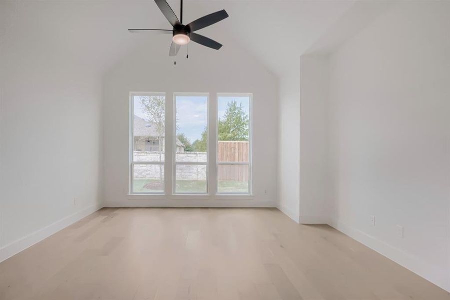 Vaulted ceiling room featuring three large windows, a ceiling fan with integrated lighting, wood-finish flooring, and white baseboards Vaulted ceiling room featuring three large windows, a ceiling fan with integrated lighting, wood-finish flooring, and white baseboards