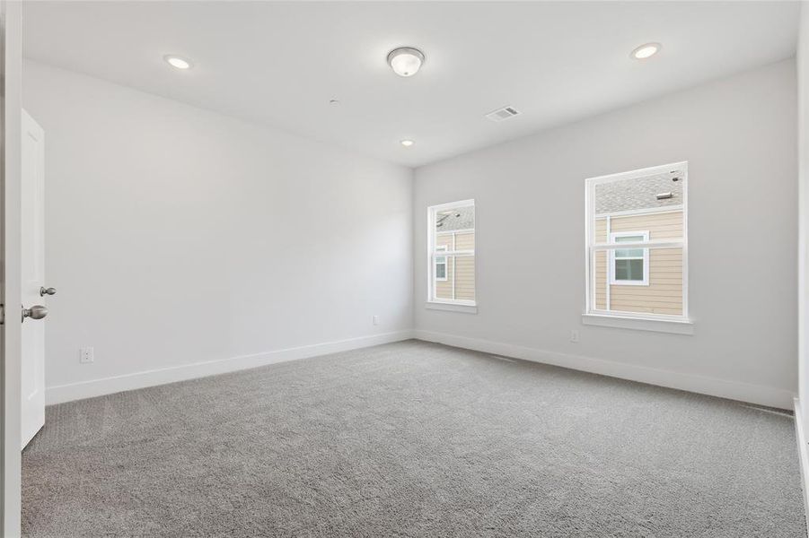 Well-lit room featuring light gray carpet, white walls, and two windows