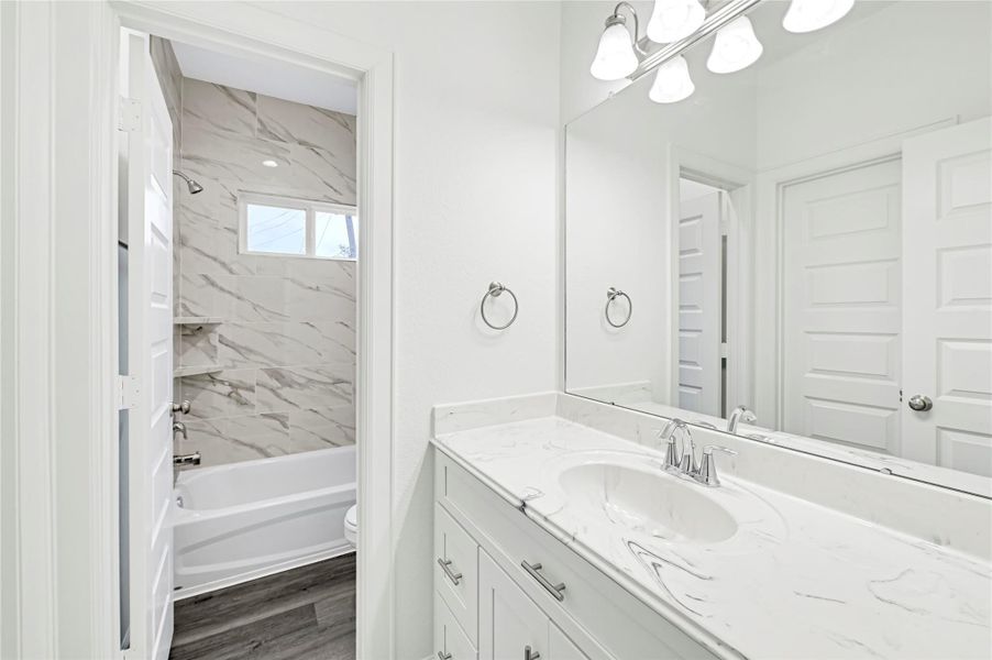 This bathroom features a modern design with a marble countertop, large mirror, and elegant lighting. It includes a bathtub with marble-style tile surround and ample natural light from a window above. The space is bright and clean with white cabinetry and fixtures. This bathroom features a modern design with a marble countertop, large mirror, and elegant lighting. It includes a bathtub with marble-style tile surround and ample natural light from a window above. The space is bright and clean with white cabinetry and fixtures.