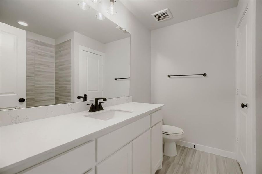 Bathroom featuring an extended vanity with a solid surface countertop and undermount sink, matte black faucet, full-width mirror, and light wood-finish floor tiling