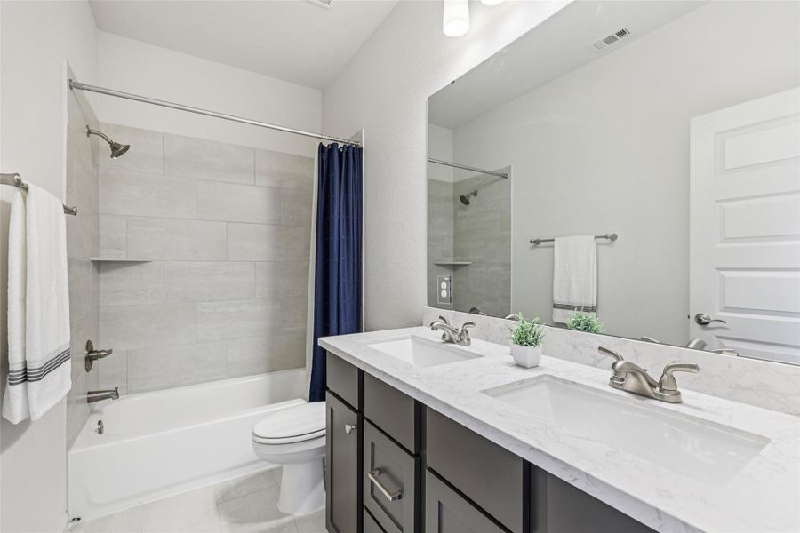 Bathroom featuring a dual vanity with white countertops, a bathtub with light gray tiled walls, and a large mirror