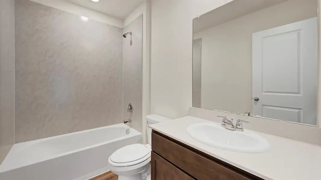 Bathroom featuring a white bathtub, light-toned shower surround, wood-finish vanity, white countertop with integrated sink, and an expansive mirror