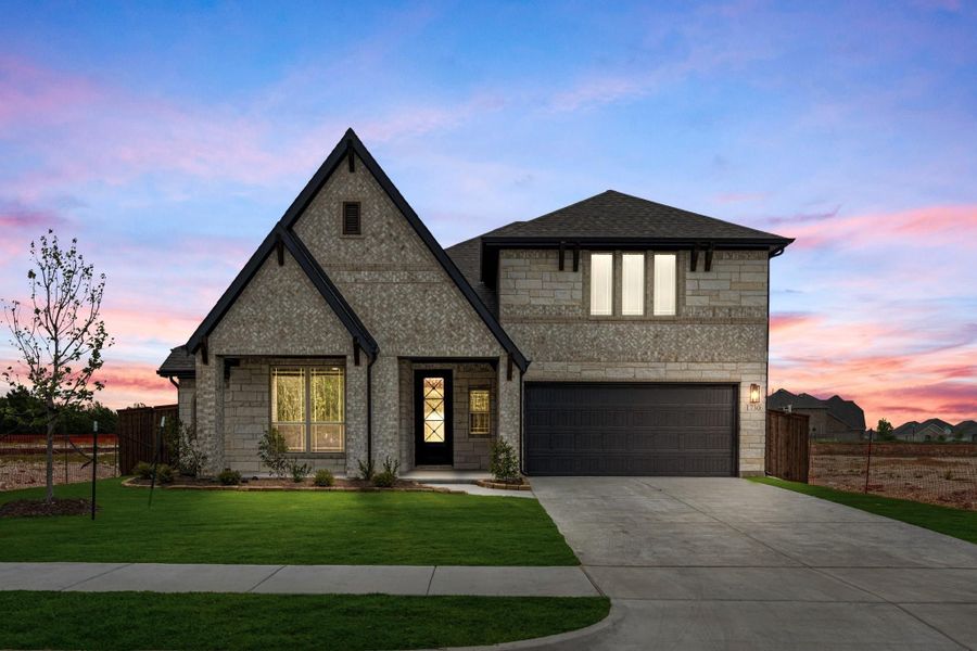 Two-story home with stone and brick exterior, dark two-car garage, steep gabled roofline, and green front lawn at dusk